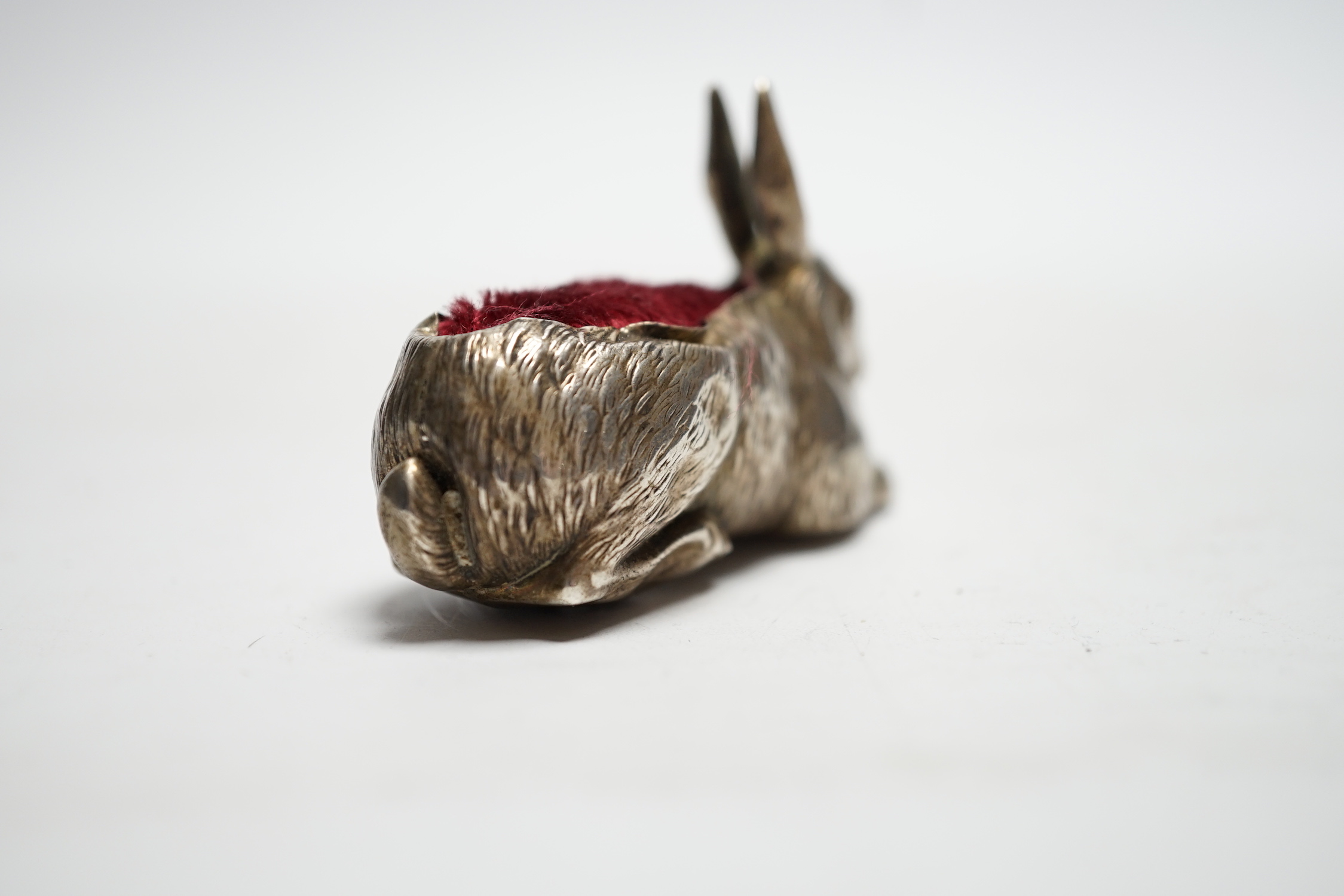 An Edwardian novelty silver mounted pin cushion, modelled as a recumbent rabbit, Henry Matthews, Birmingham, 1907, 64mm.